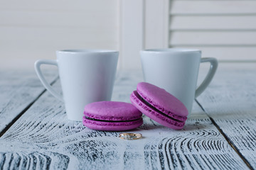 Two cups of coffee, French macaroons and an engagement ring on white wooden table. Marry me