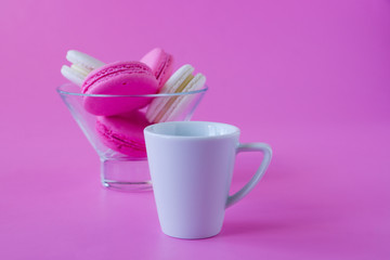 Colorful macaroons in a glass vase and cup of coffe on pink background