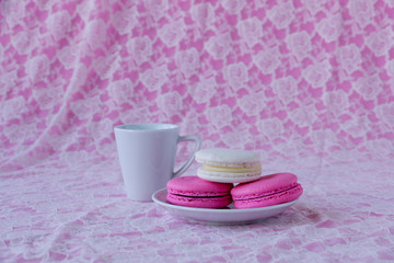 Colorful macaroons on plate and cup of coffee on white lace