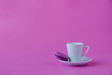 Cup of coffee and purple macaroon on pink background. Space for text
