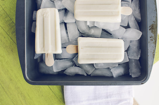 Vanilla ice cream popsicles over ice in metal tray.  