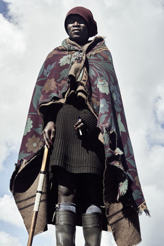 A portrait of a black Basotho shepherd against a clouded sky.
