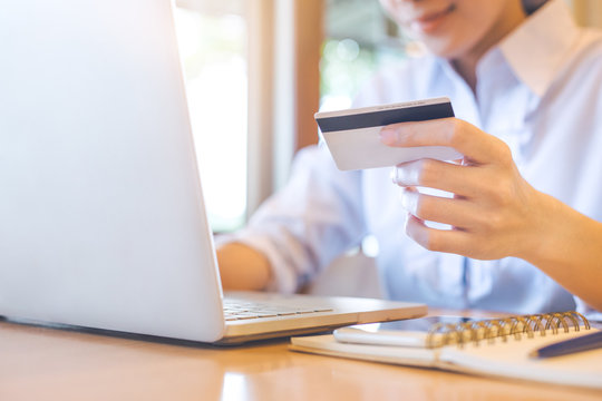 A woman's hand holds a credit card and uses a laptop to shop online.