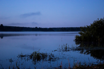 beginning sunrise on a big lake with forests and grass with beautiful mist and clouds