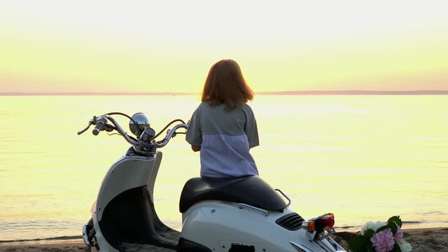 The little girl sits on the moped and watches a decline