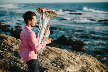Young man playing on Tuba on rocky sea coast