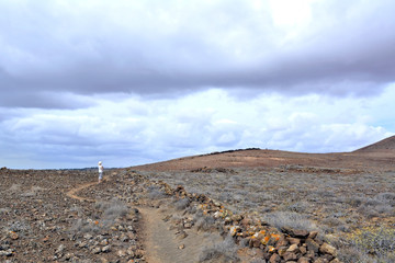 Woman walking along a path traced in a volcanic landscape.