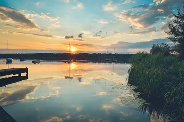 Summer afternoon landscape. Wooden pier and boat on the water at sunset.