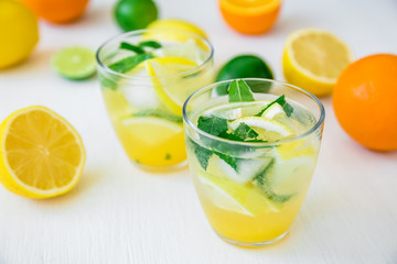 Fresh citrus lemonade with limes and lemons in glasses on white table
