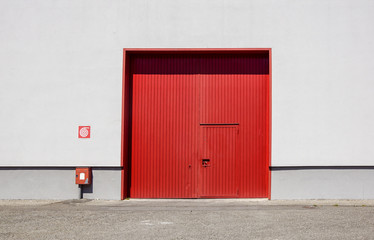 The sheet metal factory wall with the red entrance door in the industrial park.The red door of the factory building.