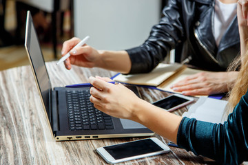 Close up of two women doing records in a notebook sitting at a laptop. Two pairs of women's hands in an office. Laptop, glasses, smartphone and notebooks are on the table. Education.