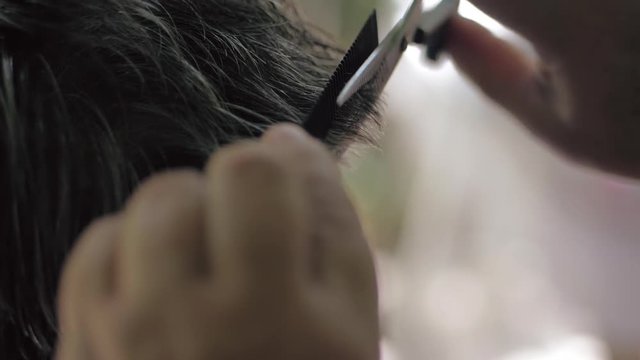 A middle-aged woman hairdresser uses scissors for cutting a brunette man with gray hair. Haircut outdoor in the summer. Close-up, slow-motion. Barber using a scissors to cut a man's hair