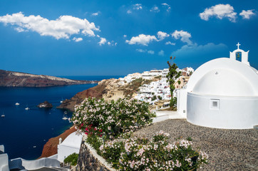 Oia Village, Santorini, Cyclade islands, Greece. Beautiful view of the town with white buildings, blue church's roofs and many coloured flowers.