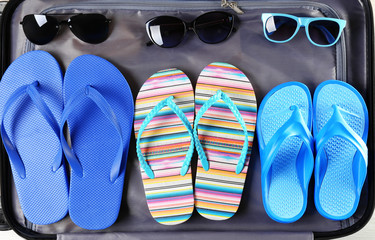 Open suitcase with flip-flops and sunglasses, closeup. Summer vacation concept