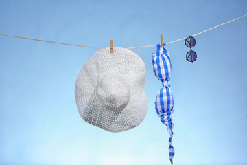Bikini bra, sunglasses and hat on rope against light color background. Summer vacation concept