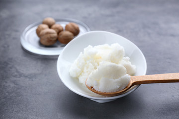 Shea butter in wooden spoon, bowl and nuts on table