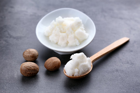 Shea butter in wooden spoon, bowl and nuts on table