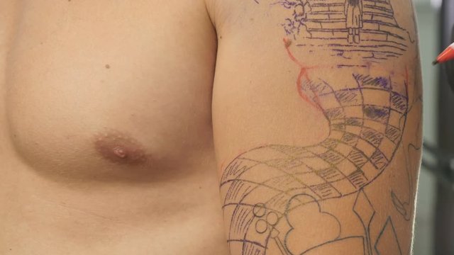 The tattoo artist draws a finishing lines of sketch on the skin before tattoing