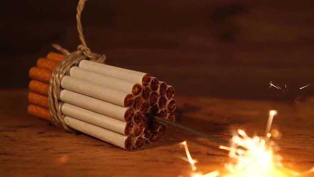 Guter Vorsatz, aufhören zu rauchen / zusammengebundene Zigaretten auf hölzernem Untergrund, mittig brennt eine Wunderkerze, Zeitlupe ohne Ton