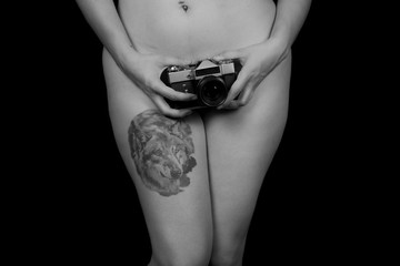 Fototapeta premium Crop shot of naked woman covering private part with vintage photo camera on black background. 