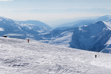 Two skiers downhill on snow off-piste slope and mountains in haze