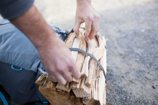 Cropped hands of hiker tying tied up firewood on bag