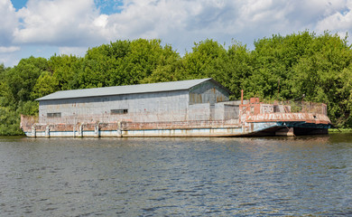 Rusty metal hangar for storage on an old barge on the river
