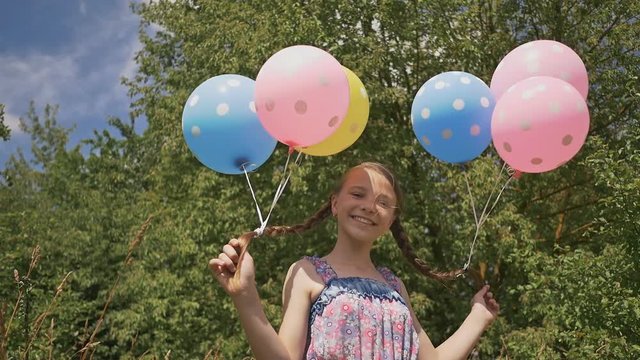 Cheerful and pretty girl with colorful balls attached to her hair and braids on her head. Funny idea with balloons.