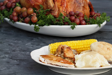 Dinner plate of roasted Thanksgiving turkey, mashed potatoes, corn on the cob, dressing and dinner rolls in front of a whole roasted turkey. 