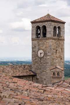 Antico campanile con orologio che svetta sopra i tetti di tegole e  vecchi camini
