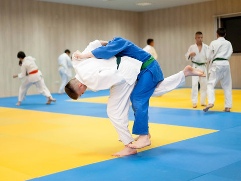 Two unrecognizable judokas fighting. Judoka in white judogi throwing attacking opponent with uchimata