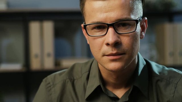 Portrait of attractive young business man in the stylish glasses looking to the camera in the modern office background.
