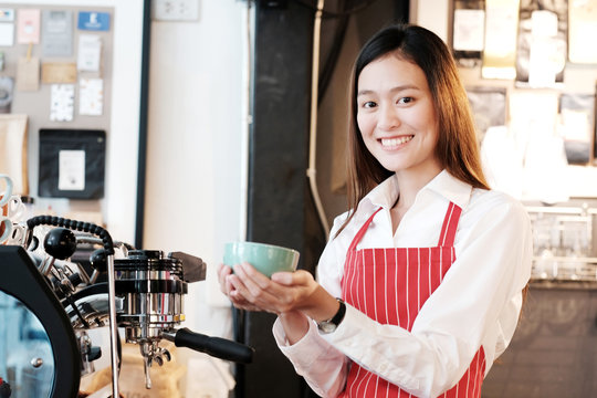 Young asian women Barista holding coffee cup with smiling face at cafe counter background, small business owner, food and drink industry concept