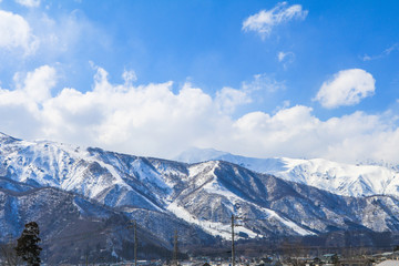 Fototapeta premium Hakuba mountain range in the winter with snow on the mountain and blue sky and clouds background in Hakuba Nagano Japan.