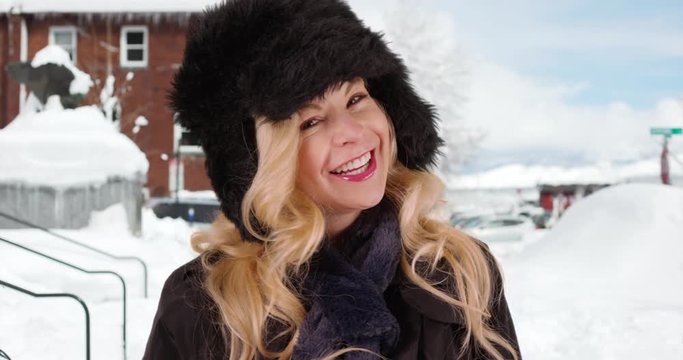 Close up of cheerful Caucasian woman in fur cap and scarf smiling at camera outdoors in snow. Close-up of attractive female on vacation enjoying cold winter. 4k 
