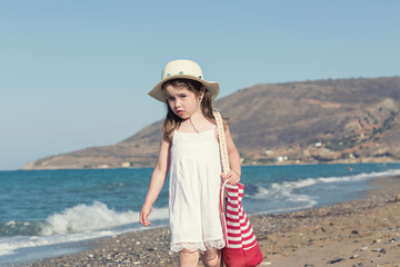 Little girl in white dress walking alone the sea, playing on the seashore