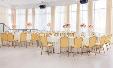 Beautifully decorated room in pastel shades of white with covered tables with flowers in the restaurant for the celebration of the wedding.