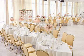 Beautifully decorated room in pastel shades of white with covered tables with flowers in the restaurant for the celebration of the wedding.