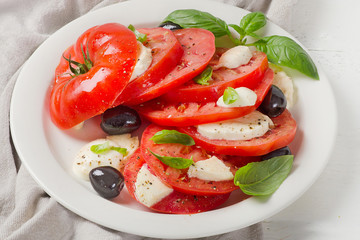 Tomato and mozzarella slices with basil leaves on a white plate.