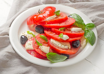 Tomato and mozzarella slices with basil leaves on a white plate.