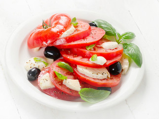 Tomato and mozzarella slices with basil leaves on a white plate.
