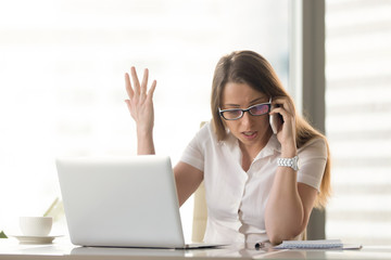 Disgruntled angry businesswoman arguing on mobile sitting at workplace, having problem of conflict...