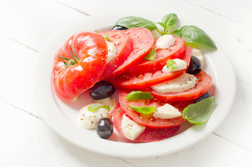 Tomato and mozzarella slices with basil leaves on a white plate.