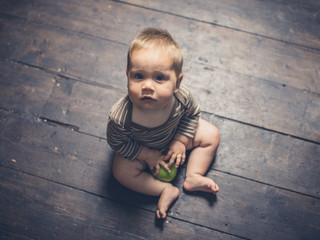 Naklejka premium Little baby sitting on floorboards with apple