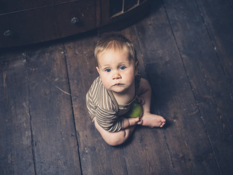 Little baby sitting on floorboards with apple