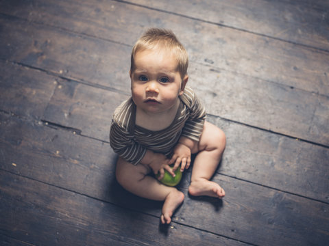 Little baby sitting on floorboards with apple