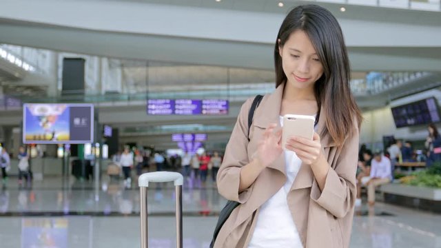 Woman go travel with her luggage and use of mobile phone in the airport