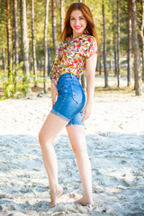 Sweet sexy girl in pin-up modern style rest on a nature, forest background. Young attractive woman in flowers shirt and blue cut shorts. Nice fashionable figure and full hips 