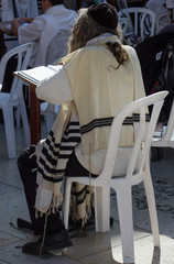 A jew in traditional dress reading torah at a holy place