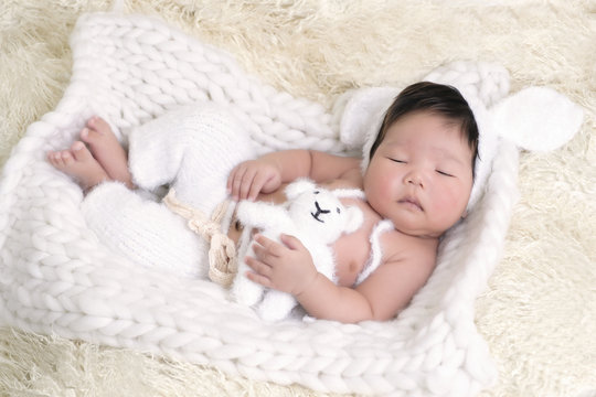 Portrait of Asia boy newborn is lay down on white fur background with bear .
